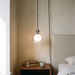 Hedda bedside pendant light hanging low beside a linen headboard over a walnut nightstand in a bone plaster bedroom