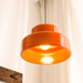 Close-up of the lit Sunna pendant, warm 2700K glow reflecting inside the orange iron shade against a white curtain