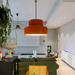 A pair of Sunna orange pendant lights lit over a kitchen island in an open-plan living room with a green sofa and cane chairs
